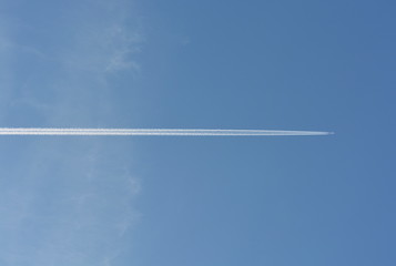 The plane flies high in the blue sky, a white trail