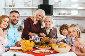 big family having thanksgiving dinner together at home and looking at camera