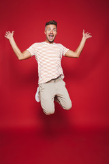 Fototapeta na wymiar Full length photo of caucasian man in striped t-shirt jumping and screaming, isolated over red background
