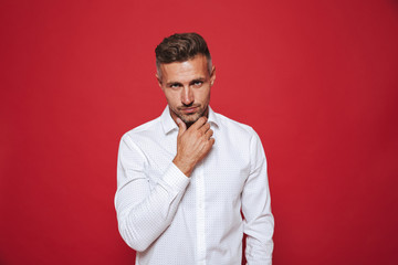 Handsome guy with stubble in white shirt looking on camera, isolated over red background
