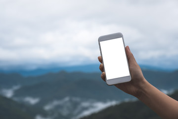 Mockup image of a hand holding and showing white smart phone with blank desktop screen in outdoor with blur green mountains background