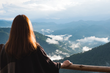 A woman standing alone and looking at mountains on foggy day with blue sky background in the morning