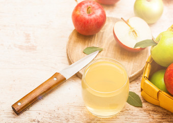 Glass of fresh organic apple juice with pink lady red and granny smith green apples on chopping board on wooden background with knife