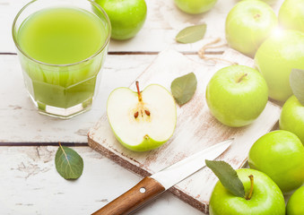 Glass of fresh organic apple juice with granny smith and british bramley apples on wooden background with sun light