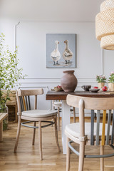 Wooden chairs at table in natural white dining room interior with poster and lamp. Real photo