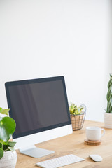 Keyboard and desktop computer on wooden desk with plants in white workspace interior. Real photo