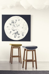 Wooden stools and moon poster in white minimal living room interior. Real photo