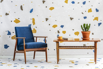 Mid-century modern, navy blue armchair and a retro wooden table in a white living room interior...