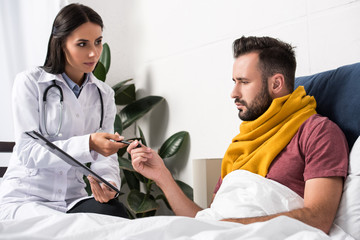female doctor giving clipboard with documents to patient while lying in bed