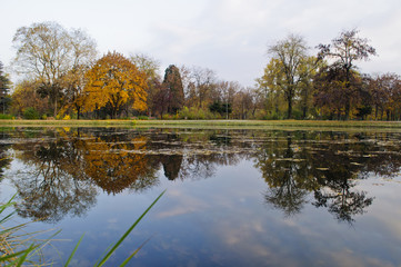 Beautiful autumn park with colorful trees and leaves and reflection in artificial ponds.