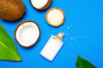 Organic cosmetics with coconut oil, ripe coconut on blue colored background top view minimal flat lay style. Coconut shavings, oil, milk. Healthy skincare. Homemade cosmetic for peeling and spa care.