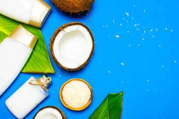 Organic cosmetics with coconut oil, ripe coconut on blue colored background top view minimal flat lay style. Coconut shavings, oil, milk. Healthy skincare. Homemade cosmetic for peeling and spa care.
