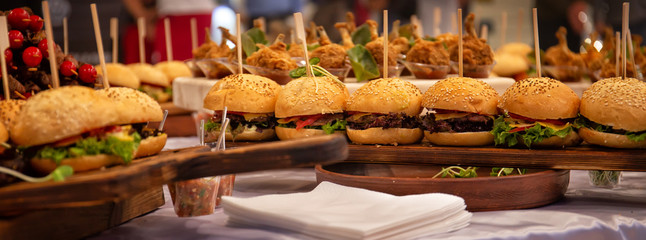 Cocktail Reception at the event, burgers, chicken legs, salads, snacks on wooden boards, with...