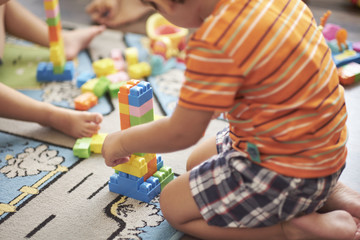 Little Asian child playing with lots of colorful plastic blocks indoor. Kid boy wearing colorful shirt and having fun with building and creating.