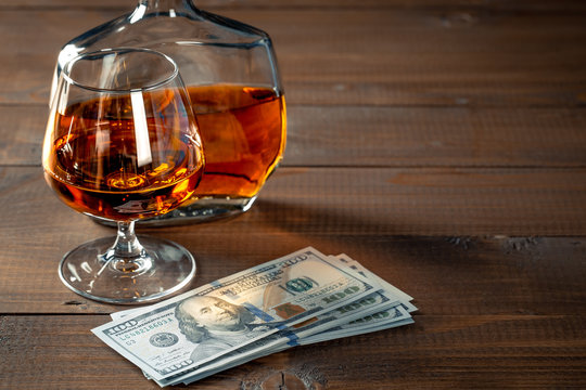 Two glasses of brandy or cognac and bottle, with wad of money on the wooden table.