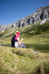 Junge blonde Frau rastet am Ufer eines Bergsees, Österreich