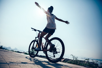 Hands free cycling woman riding mountain mike on sunrise seaside
