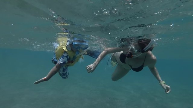 Woman and little boy in mask, snorkel and fins swim on the surface of water (underwater shot, 4K / 60fps)
