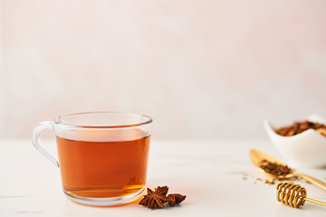 Black tea in a glass cup with golden spoon with herbs, dipper and anise on marble table top. Feminine rose background with copy space. Narrow depth of field.
