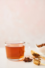 Black tea in a glass cup with golden spoon with herbs, dipper and anise on marble table top. Feminine rose background with copy space. Narrow depth of field.