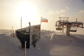 The Russian flag is developing in bad weather at the top of the mountain with a ski lift