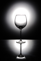 Transparent empty wine glass on a black background with white backlight on a mirror surface