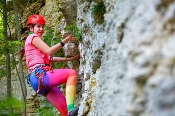 Photo from back of sports woman in red helmet climbing up mountain to top