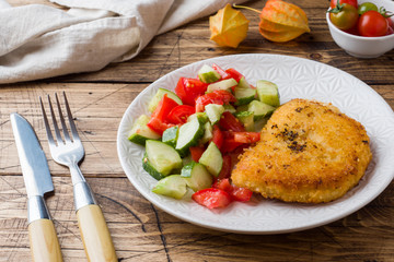Chicken cutlet and cucumber salad with tomatoes on a wooden table