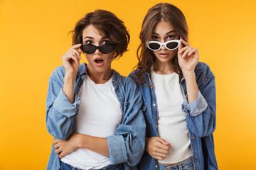 Excited emotional young women friends posing isolated over yellow background.