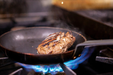 Chef seasoning beef on pan while cooking in restaurant kitchen