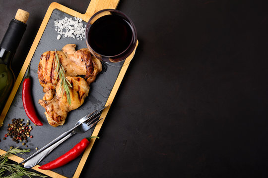 Grilled chicken fillets on slate plate with rosemary, wine and spices on dark wooden background. Top view. Flat lay. Copy space