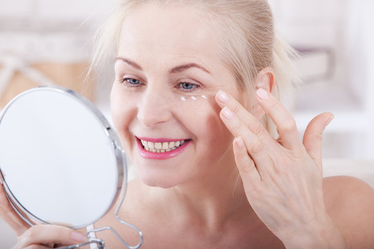 Middle aged woman looking at wrinkles in mirror. Plastic surgery and collagen injections. Makeup. Macro face. Selective focus
