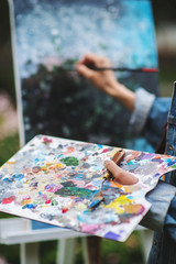 Art, creativity and people concept - close up of artist with palette and brush painting still life on paper at studio outdoor. Picture of field flowers
