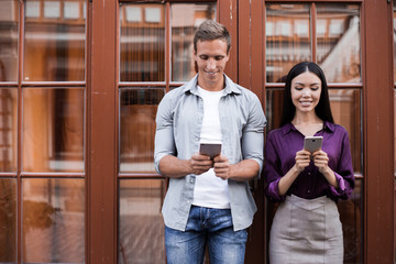 Male and female hipsters walking on grey wall background ignoring each other preferring social networks,students chatting online instead of communicating in real life strolling pon publicity area