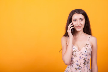 Fototapeta premium Beautiful young woman talking on her phone in studio over yellow background.