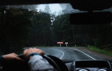 Driver's hand on a steering wheel inside a car on a road
