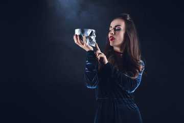 beautiful vampire holding metal skull on dark background with smoke