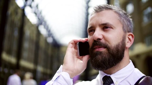 Businessman with smartphone on the trian station in London, making a phone call.