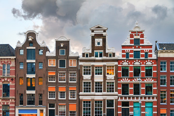 Naklejka premium Fasady typowych holenderskich dworków nad kanałami światowego dziedzictwa UNESCO w Amsterdamie w Holandii, z letnim niebem o zachodzie słońca