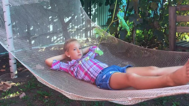 Cute child girl lying on hammock and relax at the garden.