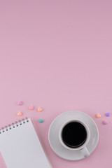A cup of coffee and blank notebook decorate with pastel heart pattern on pink background with copy space