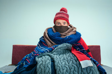 Bearded sick man with flue sitting on sofa at home or studio covered with knitted warm clothes....