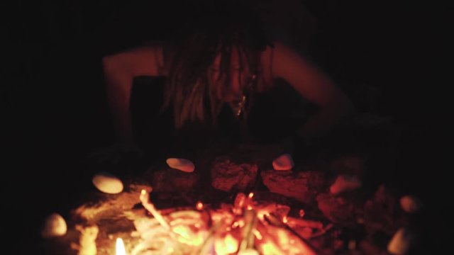 Scary witch does voodoo black magic ritual near the fire at night. Halloween horror 