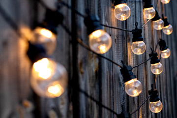 Lots of warm LED light bulbs on old wooden background in the garden, copyspace, outdoor lighting...