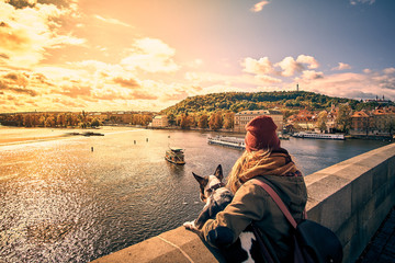 Young women tourist with a puppy dog and a backpack looking at the tourist boat and swans sailing on Vltava river from the Charles Bridge (Karluv Most) in Prague, Czech Republic - 223171369