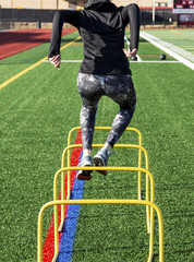 Female jumping over mini hurdles from behin