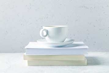 A white cup of coffee or tea on a stuck of books. Copy space. Gray background