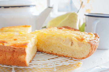 Pie from the cottage cheese pastry with pear and sour cream, cut into pieces on a white table, horizontal