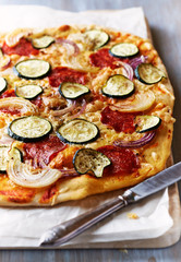 Home made thin crust pizza with salami, zucchini, onion and mozzarella. Close-up