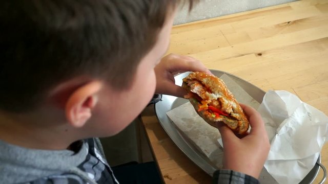 A teenager in a cafe eating a hamburger. He is hungry, View from the top